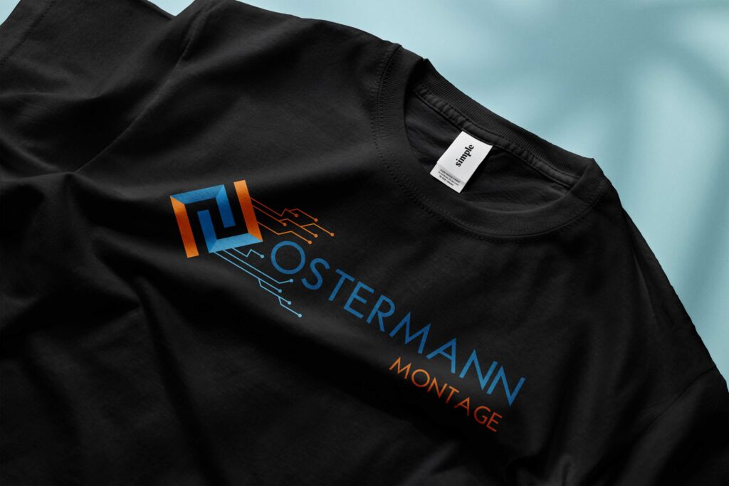 Das Bild zeigt einen Ausschnitt von einem schwarzen T-Shirt, welches mit dem Logo der Firma "Ostermann Montage" bedruckt wurde. Das Logo ist in den Farben blau und Orange, während der Hintergrund, auf welchem das T-Shirt präsentiert wird, hellblau ist.